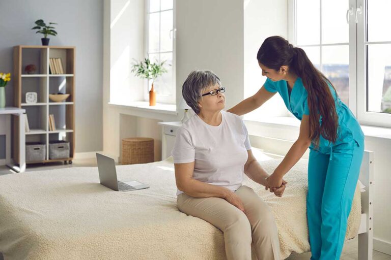 Older adult arranging labeled clothing, toiletries, family photos, and a walker in a bright assisted living room.
